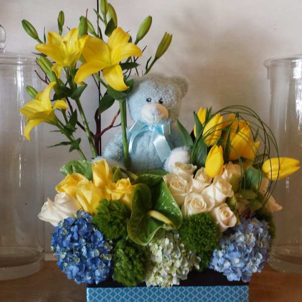 Yellow lilies and roses arranged with a blue teddy bear in a box