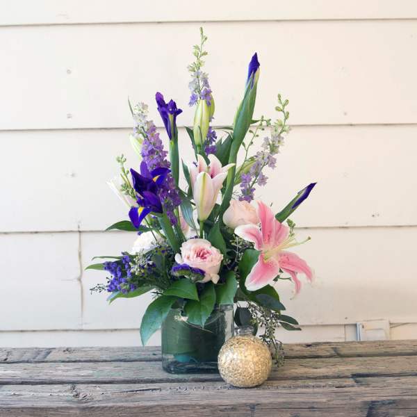 Mixed bouquet of pink lilies, purple irises, and roses in a glass vase