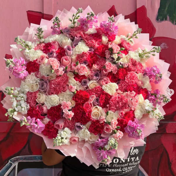 Large bouquet of pink, red, and white flowers wrapped in pale pink paper