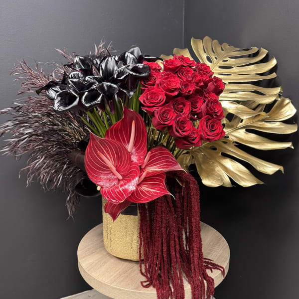 Dramatic arrangement of red roses, black calla lilies and tropical blooms in a gold vase with gold leaves