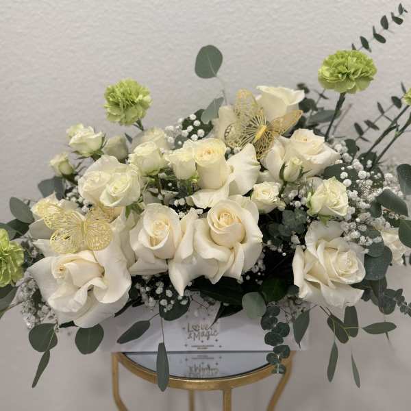 White roses and green carnations arranged with eucalyptus in a box