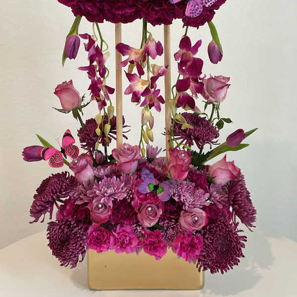Magenta floral arrangement with tulips, roses, and butterflies in a gold vase