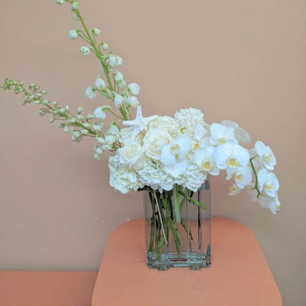 White floral arrangement in a clear glass vase with orchids and roses
