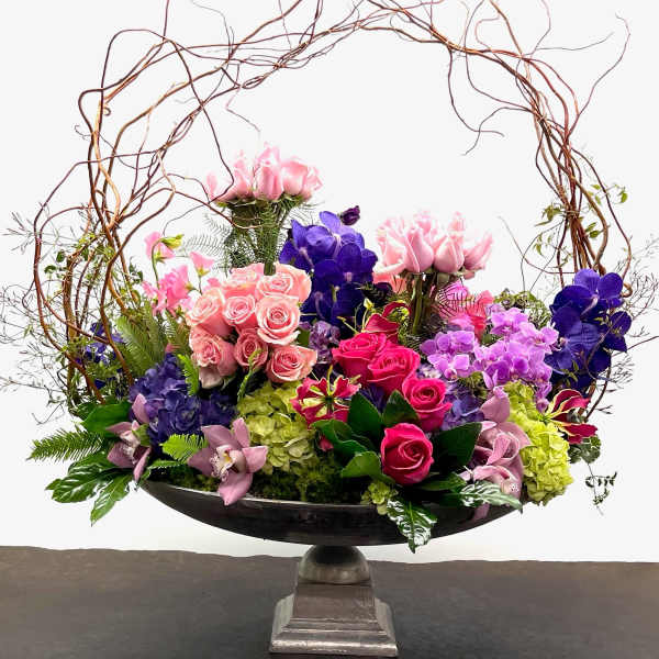 Large floral arrangement with pink, purple, and green blooms in a pedestal bowl