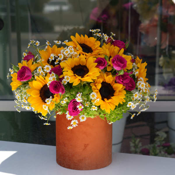 Sunflowers, pink roses, and white daisies in a tall orange vase