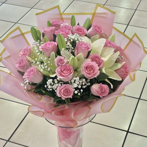 Hand-tied bouquet of pink roses, white lilies, and baby's breath wrapped in pink paper.