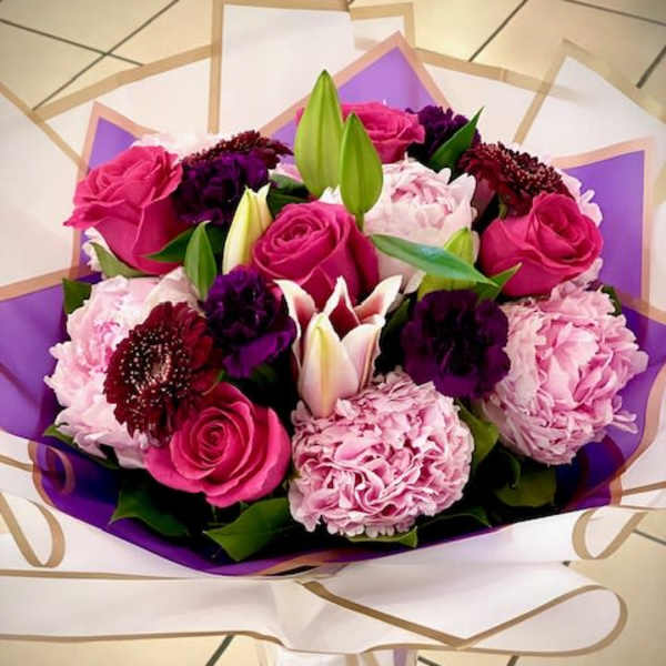 Bouquet of pink roses, lilies, and purple flowers wrapped in white and purple paper