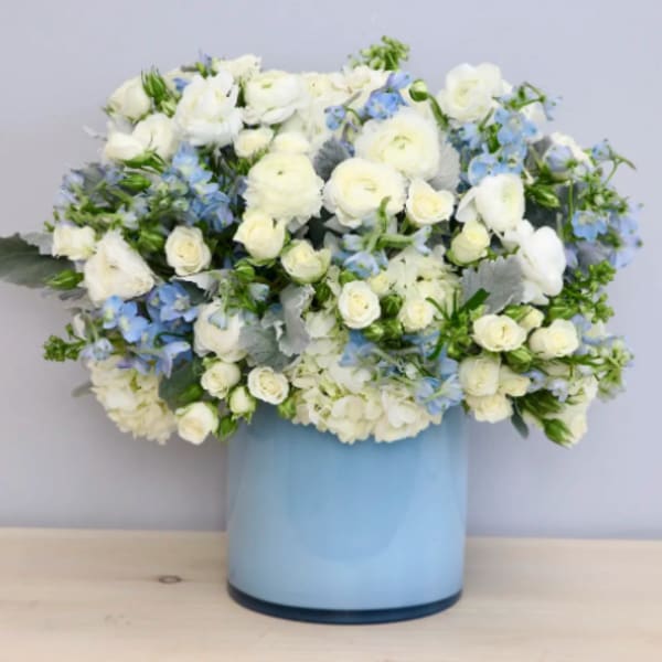 White roses and blue flowers in a light blue vase