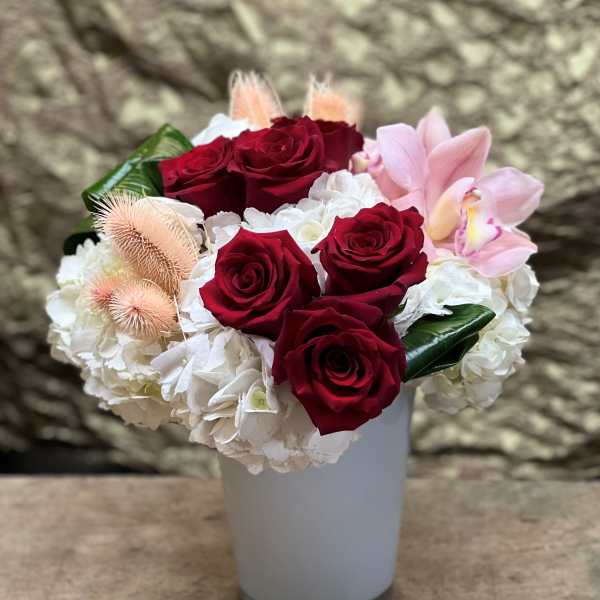 Red roses and white hydrangeas in a white vase with pink orchids