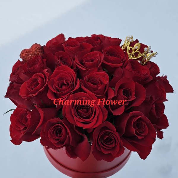 Red roses arranged in a round red box with a small crown decoration