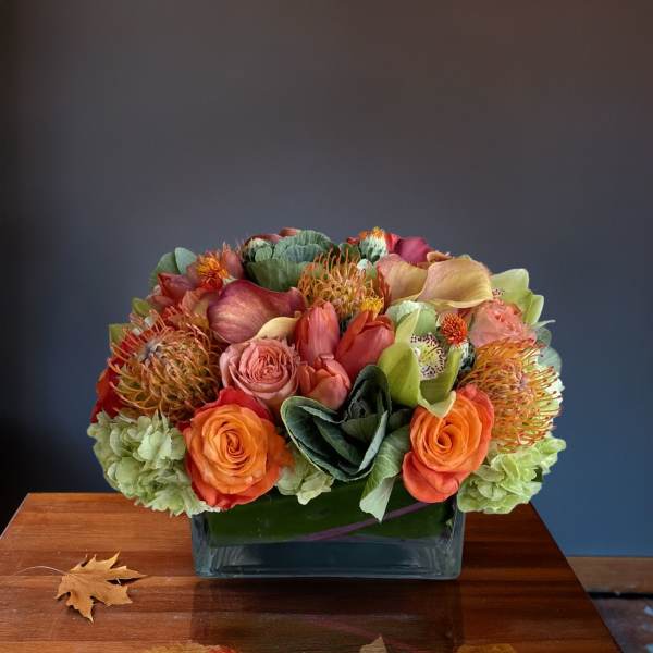 Low floral arrangement in a glass vase with orange, pink, and green blooms