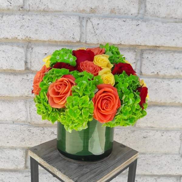Bouquet of orange and red roses with bright green hydrangeas in a glass vase