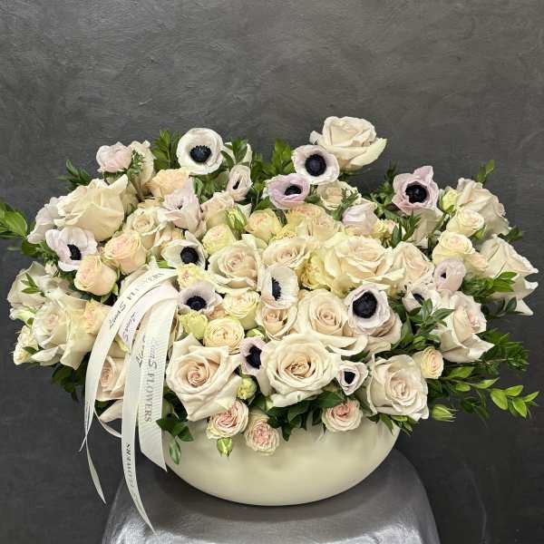 Cream rose arrangement in a low white vase with pale anemones