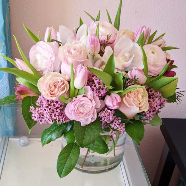Pink and white bouquet of roses, tulips, and orchids in a glass vase