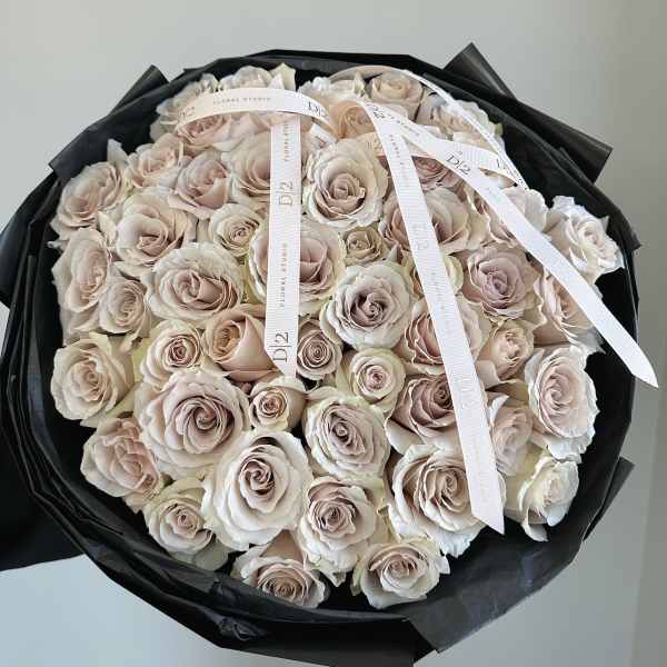 Bouquet of pale blush roses wrapped in black paper with white ribbons
