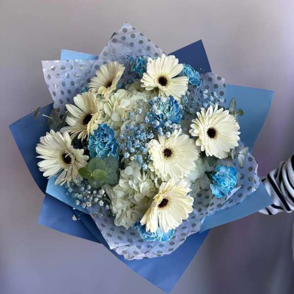 Hand-tied bouquet of white gerbera daisies and blue flowers wrapped in blue and polka dot paper