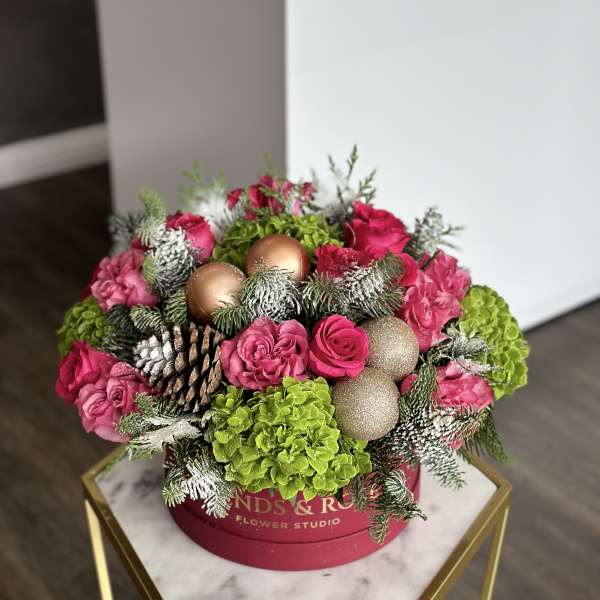 Pink roses and green hydrangeas in a round box with pinecones and ornaments