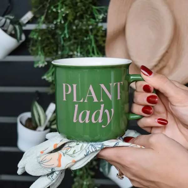 Green mug with "PLANT lady" text held over a floral cloth