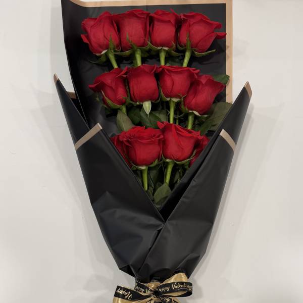 Bouquet of red roses wrapped in black paper with a gold ribbon
