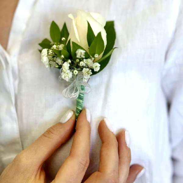 White rose boutonniere with baby's breath and green leaves