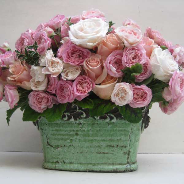 Pink and white roses arranged in a green ceramic container