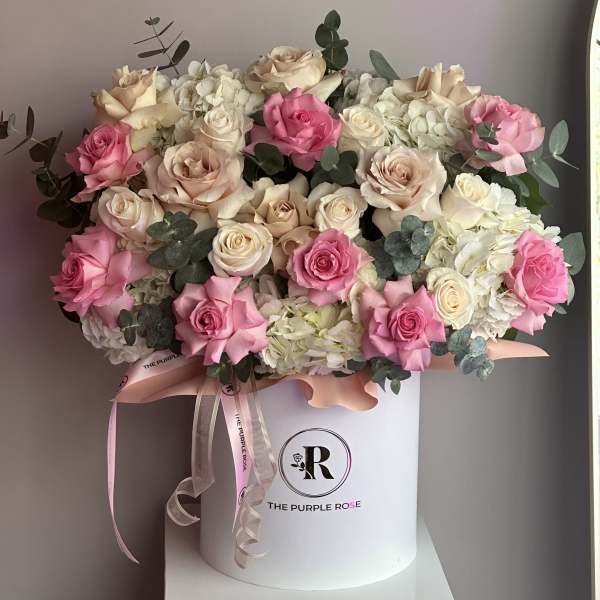 Pink and cream roses with white hydrangeas arranged in a white hatbox with ribbons