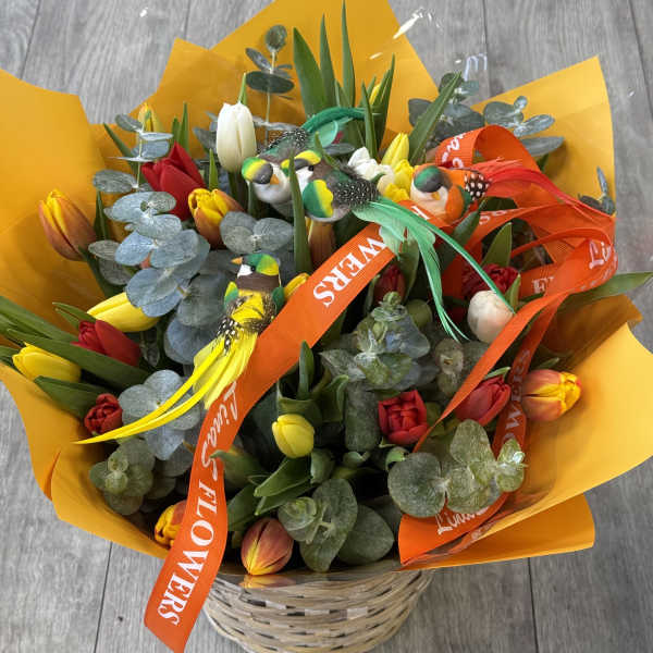 Bouquet of multicolored tulips in a wicker basket with bird decorations