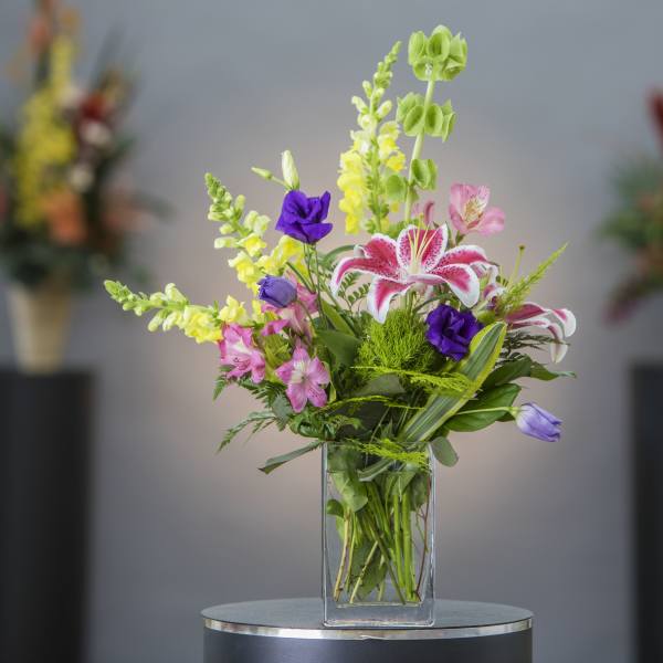 Mixed bouquet in a clear glass vase with pink, yellow, purple, and white flowers