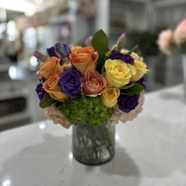 Mixed roses in orange, yellow, purple, and pink in a glass vase