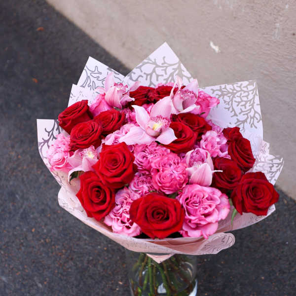 Bouquet of red and pink roses with pale pink orchids in a glass vase