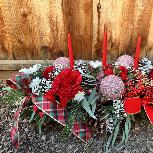 Holiday floral centerpiece with red candles, red flowers, and plaid ribbon