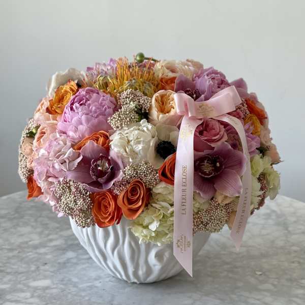 Mixed bouquet of pink, orange, and white flowers in a white vase