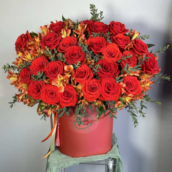 Large arrangement of red roses and orange alstroemeria in a red hatbox-style container