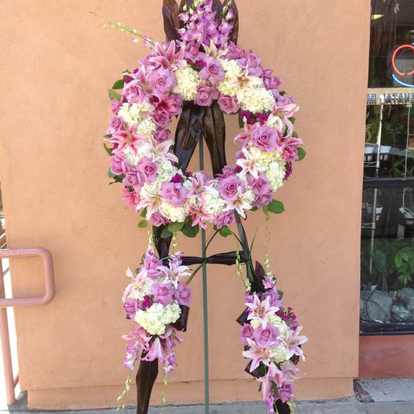 Standing floral wreath with pink roses, lilies, and white blooms on an easel