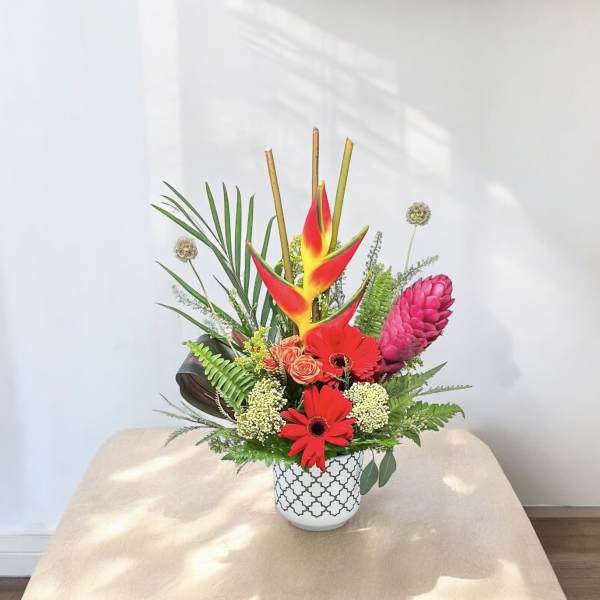 Tropical flower arrangement in a patterned white vase with red and pink blooms