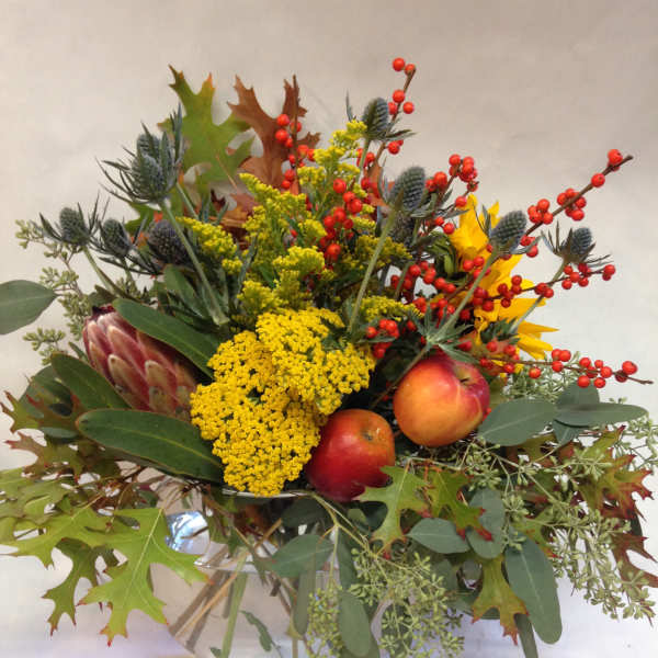 Autumn bouquet with yellow flowers, red berries, and apples in a glass vase