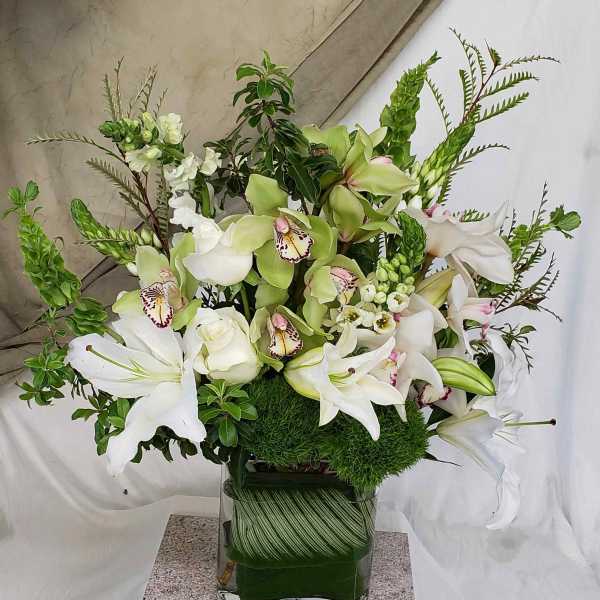 White lilies and green orchids arranged in a square glass vase.