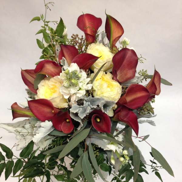 Bouquet of burgundy calla lilies and pale yellow roses with trailing greenery