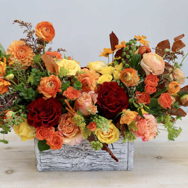 Mixed orange, yellow, and red floral arrangement in a rustic wooden box