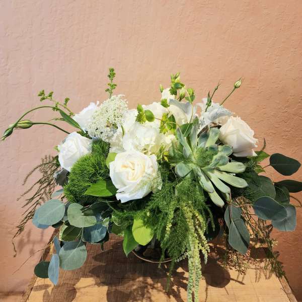 White roses and succulents in a low arrangement with greenery