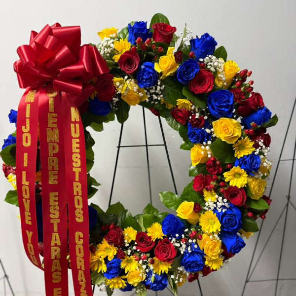 Circular floral wreath with red, blue, and yellow roses and a large red bow