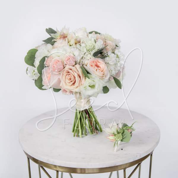 Blush and white bridal bouquet with matching boutonniere on a table