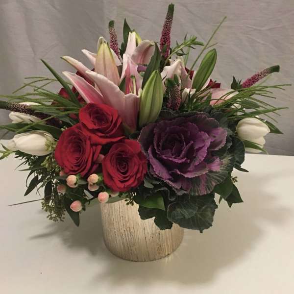Mixed bouquet of red roses, pink lilies, and purple ornamental cabbage in a vase