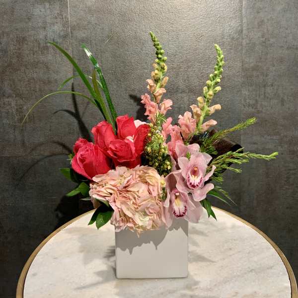 Pink roses and orchids arranged in a white square vase