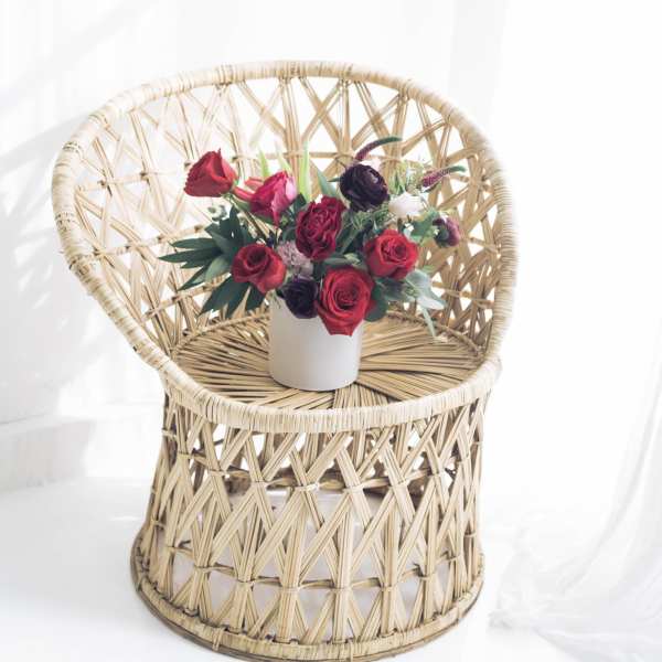 Red rose arrangement in a white vase on a wicker chair