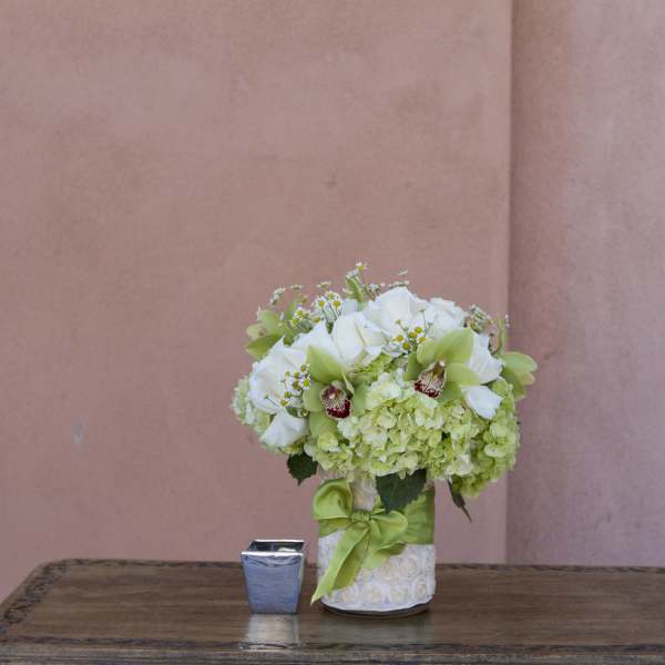 White and green floral arrangement in a decorated vase with a green ribbon