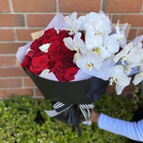 Bouquet of red roses and white orchids wrapped in black paper