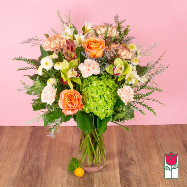 Mixed bouquet of orange roses, green hydrangea, and assorted flowers in a clear glass vase