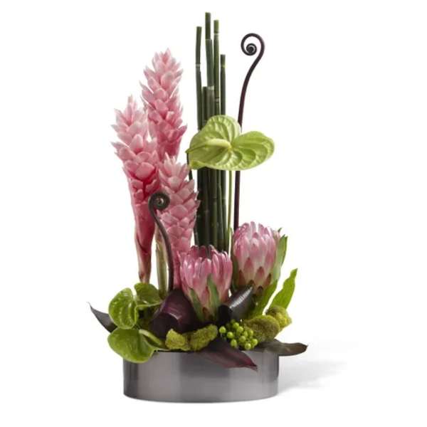 Pink tropical flowers in a low gray container with bamboo accents