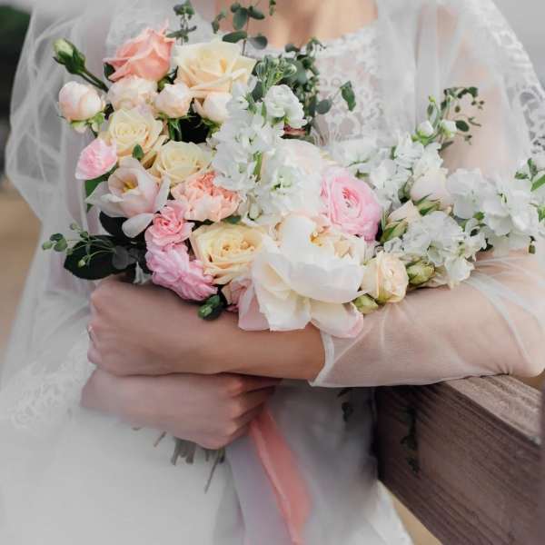 Bride holding a pastel bouquet of roses, ranunculus, and white blossoms